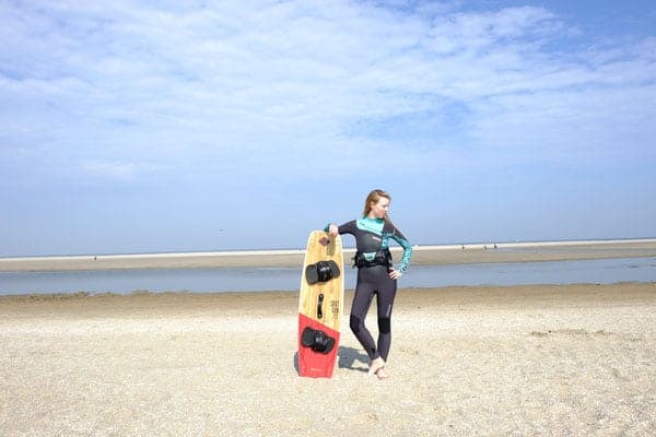 surfing paulina, standing with arm on surfboard in surf gear in algarve