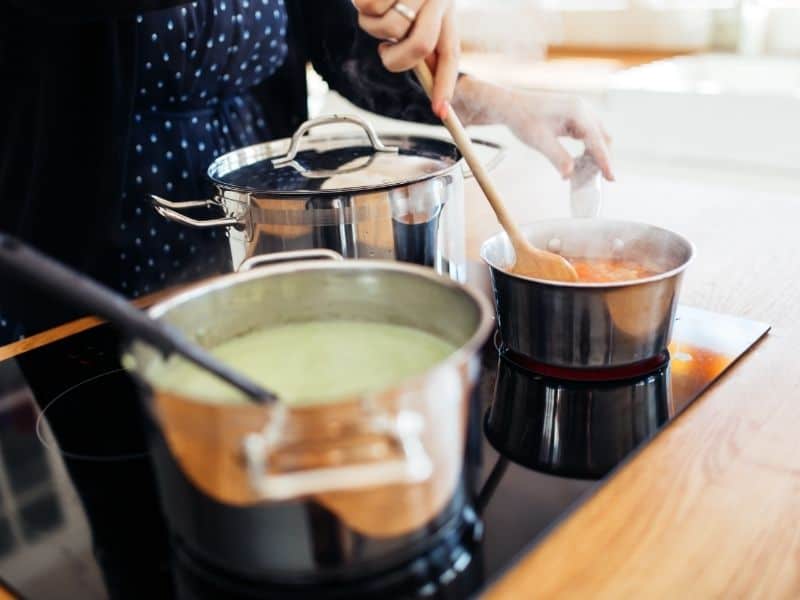 what to do in Wisconsin in February, 2 pans on with soup being cooked, with a woman holding a ladle on one hand and an ingredient on the other