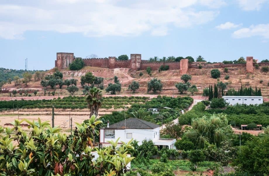 ruins of the castle of silves in distance behind homes and greenery