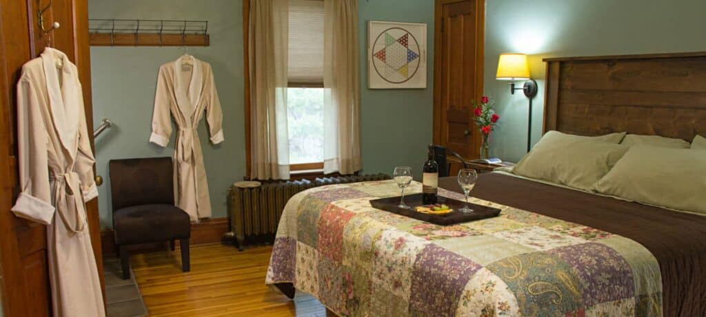 best couples hotels Wisconsin, bed with a tray that has wine bottle, two wine glasses and fruit, robes hanging in background