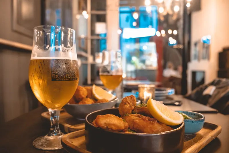 best restaurants in bruges, two wooden trays with bowls of battered snacks topped with lemons next to beers