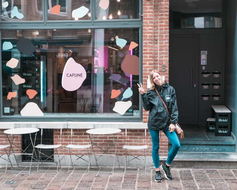 coffee shops in bruges belgium, person posing with a peace sign in front of a cafe that reads 'cafune'