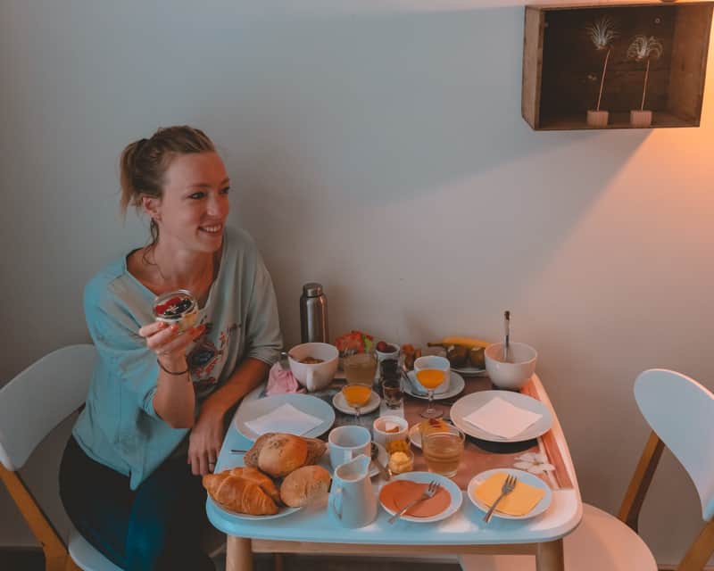 where to eat in bruges, smiling person sitting down enjoying a spread of breakfast foods