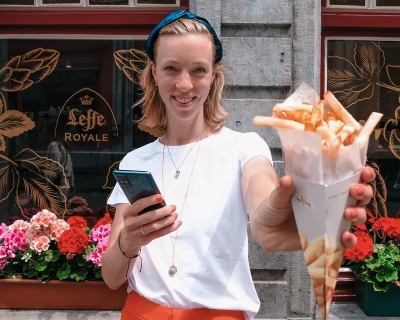 best fries in bruges, holding out a sleeve of french fries in front of a restaurant