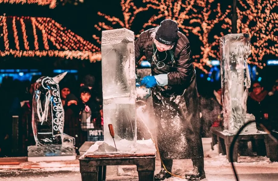 winter festivals in wisconsin, man carving ice with peopple and winter lights at the back
