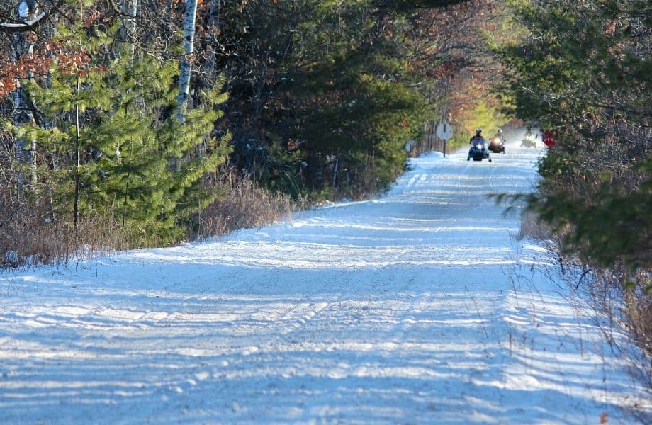 people snowmobiling in Minocqua with a road filled with snow and trees lining on the side