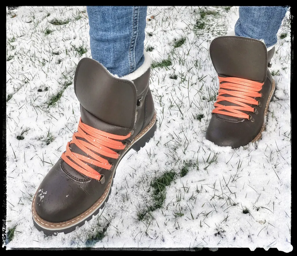 warm vegan winter boots for women, person walking in snow in brown winter boots with orange laces