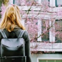 best brands to buy vegan backpacks, woman wearing a Matt & Nat vegan leather backpack and looking at flower clossoms