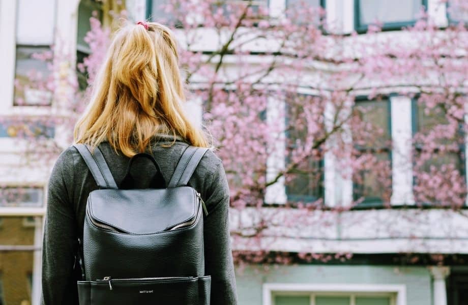 best brands to buy vegan backpacks, woman wearing a Matt & Nat vegan leather backpack and looking at flower clossoms