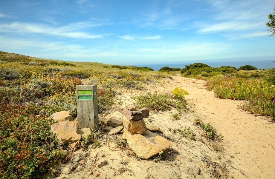 best algarve hiking trails, trail marker and sandy path under bright blue sky on Cabo de Sao Vicente Sagres hiking trail