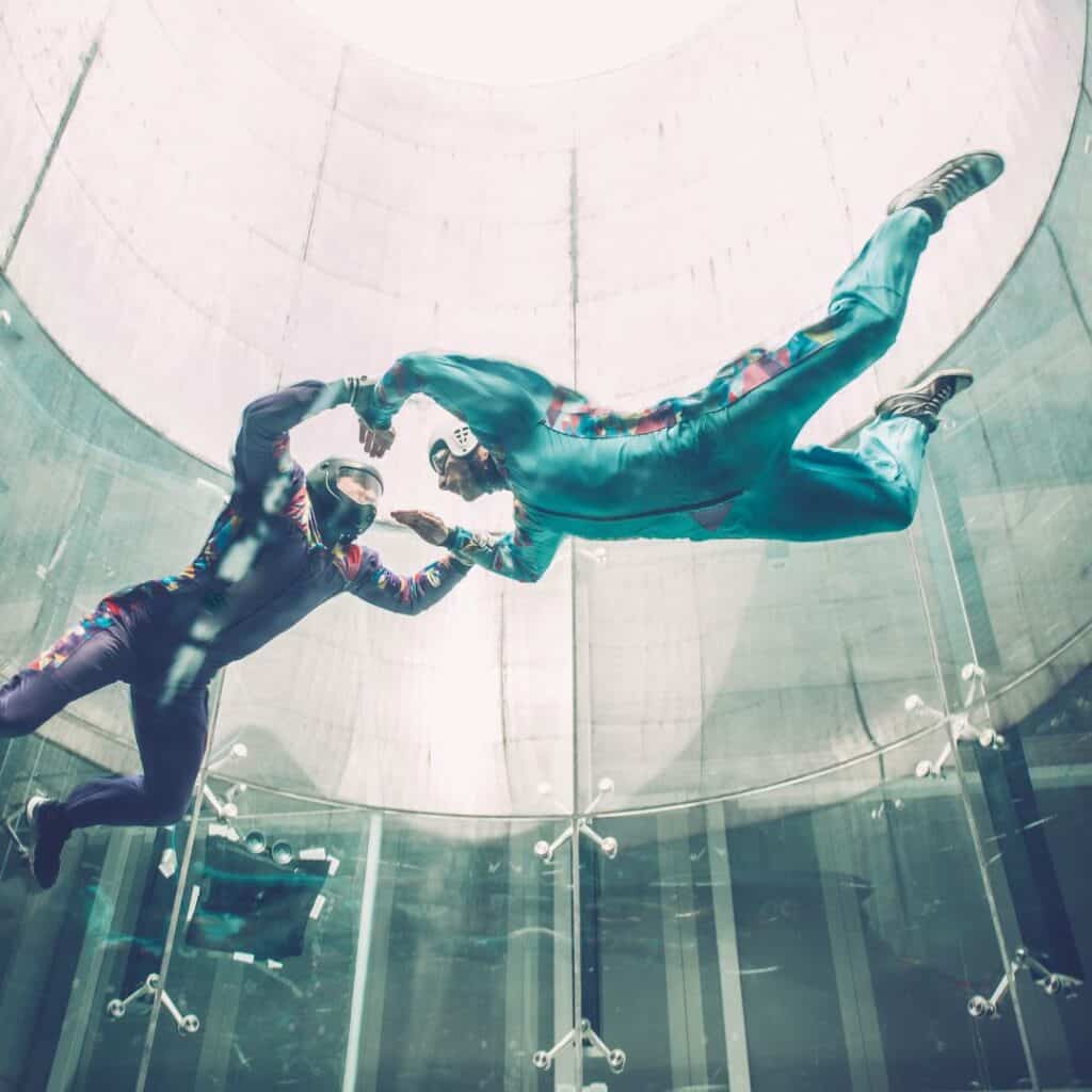 two people in the air doing indoor skydiving in a large glass structure