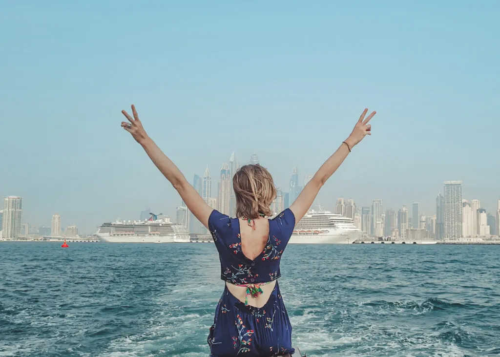 a woman on her back raising her arms with a peace sign and a body of water and buildings at the back, Cool Travel Quotes in Spanish