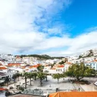 Best things to do in Albufeira, Portugal, view out onto courtyard with trees and white stone tiles surrounded by white buildings with terracotta rooftops under a blue sky with clouds