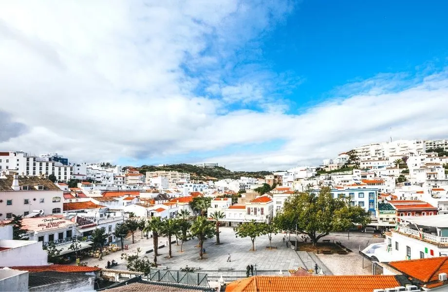 best Lagos Portugal excursions, , view out onto courtyard with trees and white stone tiles surrounded by white buildings with terracotta rooftops under a blue sky with clouds