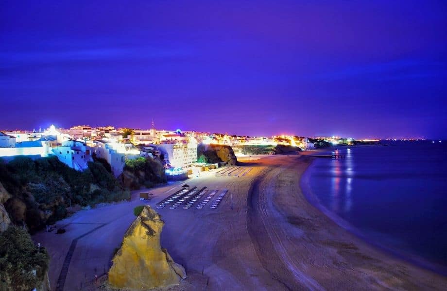 top things to do in Albufeira at night, beach at night with city lit up just beyond the beach