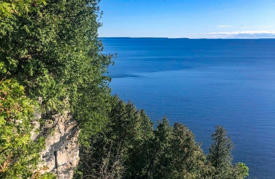 Door County hiking trails, view from Ellison Bluff with bit of tree covered cliff face and clear blue water stretching for miles