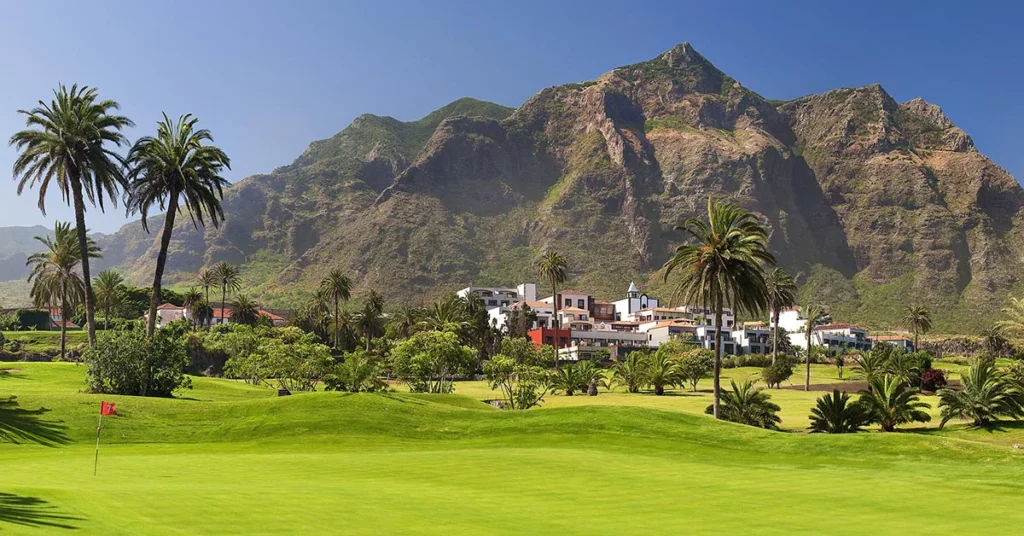 Best luxury Tenerife spa hotels, exterior view of hotel with traditional Spanish architecture surrounded by trees and golf course with mountains just behind