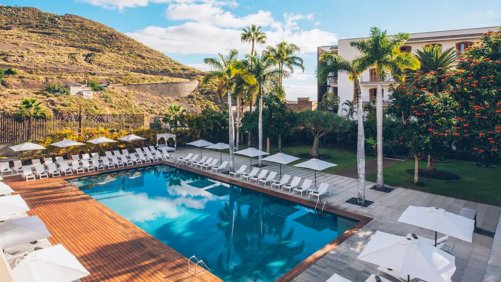 large pool surrounded by pool chairs and hotel with a view of the mountains and ocean on one side, where to stay in tenerife in December