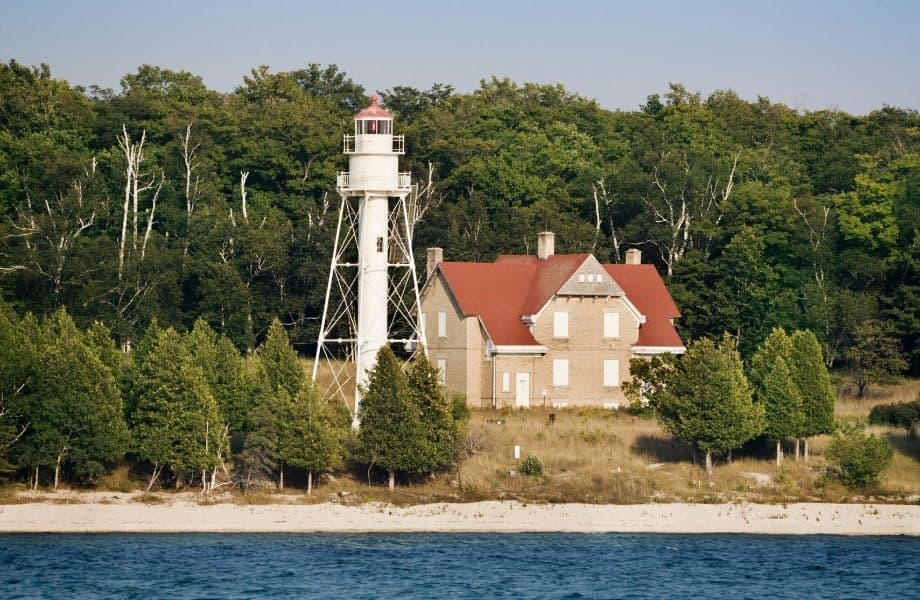 best Door County hiking trails, house and lighthouse surrounded by trees near sandy coastline