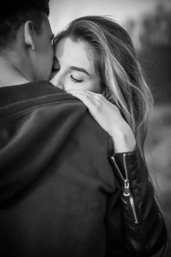 a black and white picture of a girl hugging his boyfriend while he faces her
