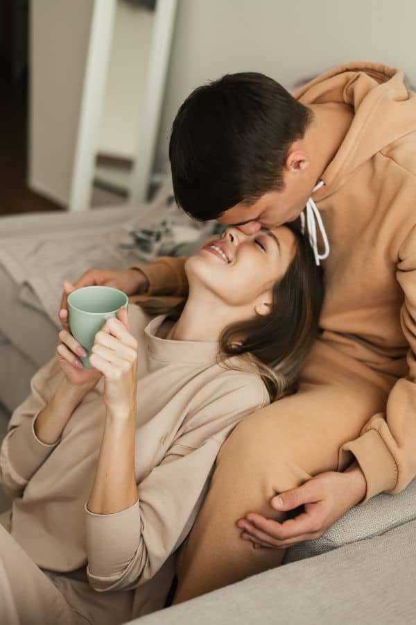 a man kissing his girlfriend's forehead while the girlfriend is looking up and holding a cup of coffee at one of the most romantic hotels in Door County