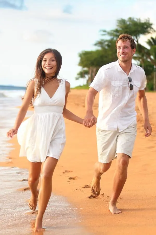 A couple holding hands while running to the beach