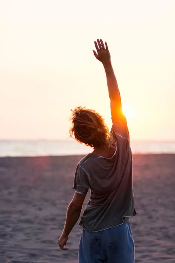 a woman raising her hand feeling free on a beach during sunset