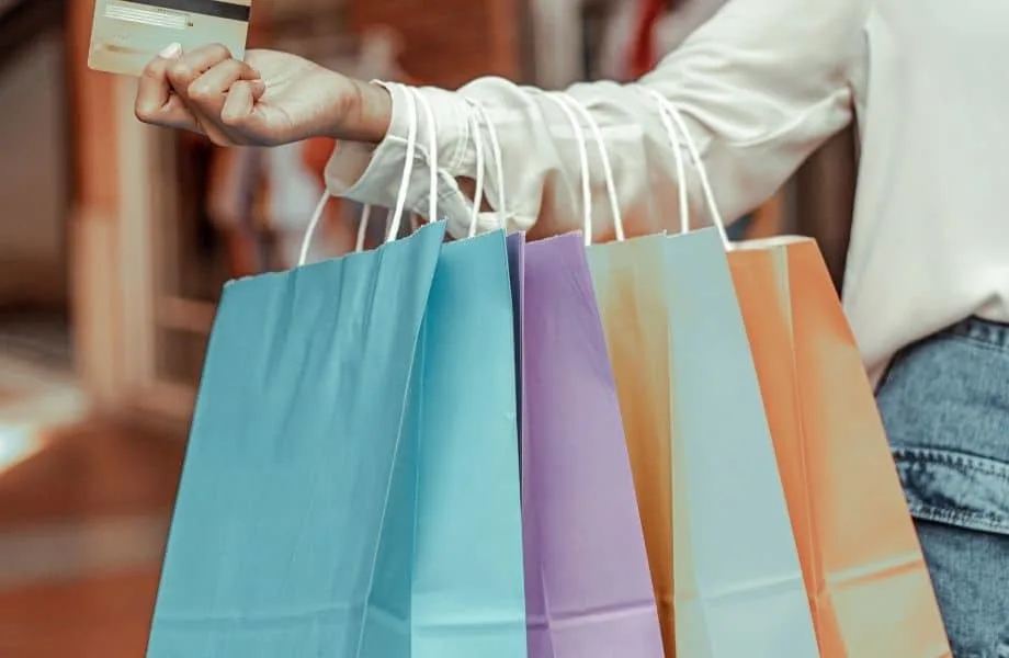 woman holding out her credit card with four colorful paper bags hanging from arm while shopping in lake geneva, wisconsin
