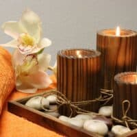 Best Spa Hotels in Tenerife, three lit candles surrounded by round rocks, an orange towel and some flowers
