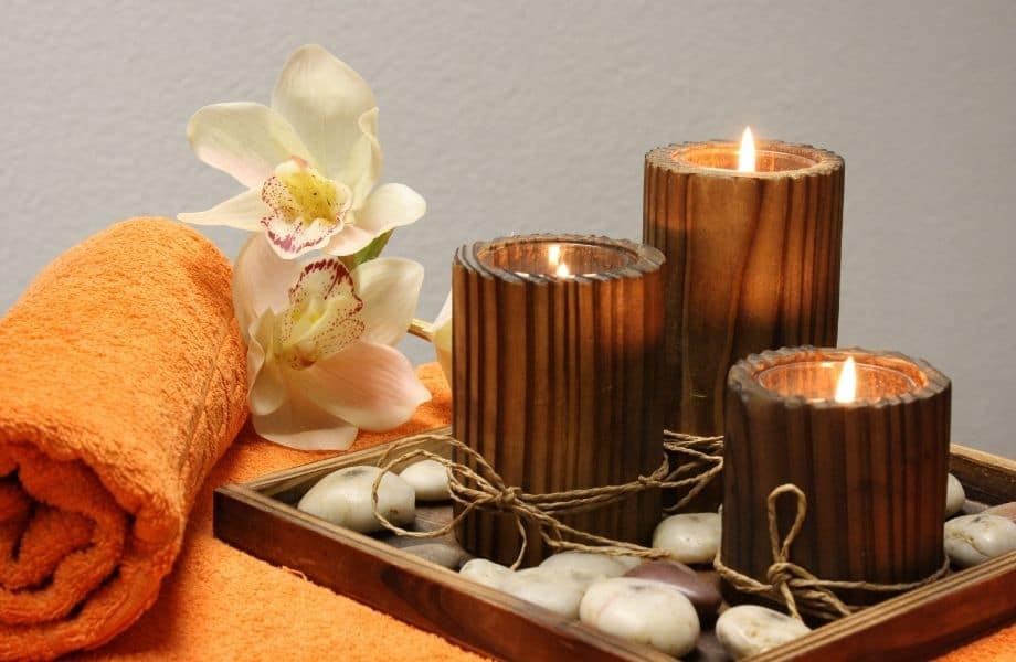 Best Spa Hotels in Tenerife, three lit candles surrounded by round rocks, an orange towel and some flowers