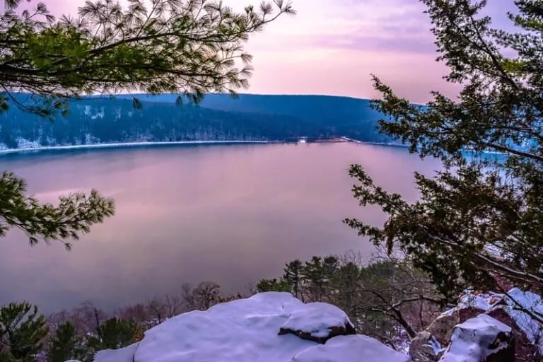 best places to visit in the winter in Wisconsin, view from hillside of a large frozen lake surrounded by rolling hills covered in snow and green trees