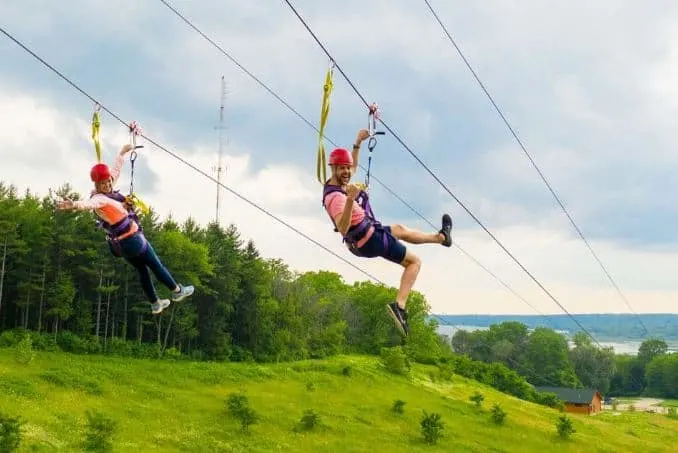 fun things to do in Door County in February, two smiling people zip lining near a forest towards nearby lake