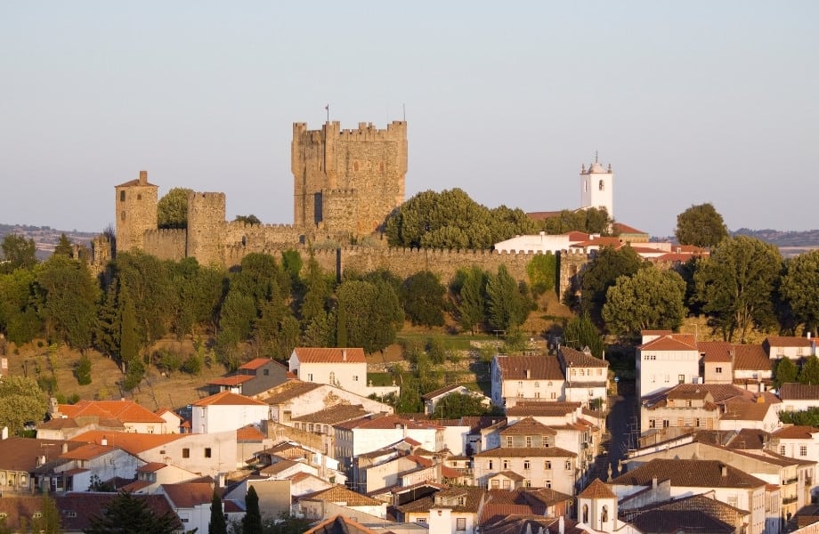 Best places to visit in north Portugal, old stone castle with white bell tower surrounded by green trees and with many white buildings with brown roof tiles in the foreground
