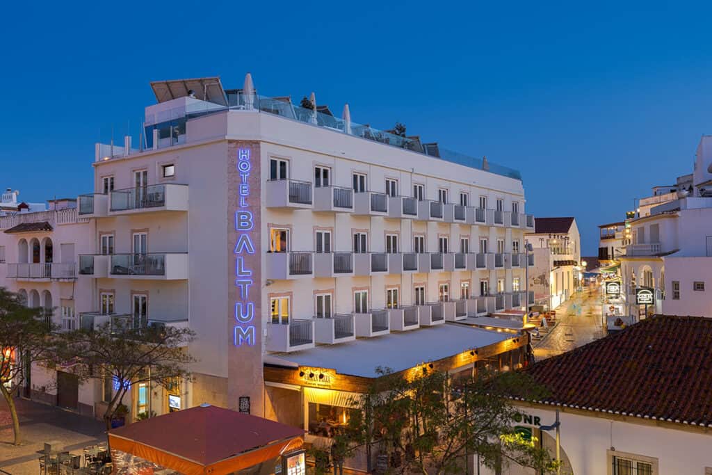 top Albufeira accommodation, exterior of Hotel Baltum at night with name down the side of the building in neon lettering and lit up street beneath