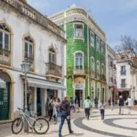 places to visit in Lagos, Portugal, people walking through large open stone square next to old white building with awnings and tall green tiled historic building