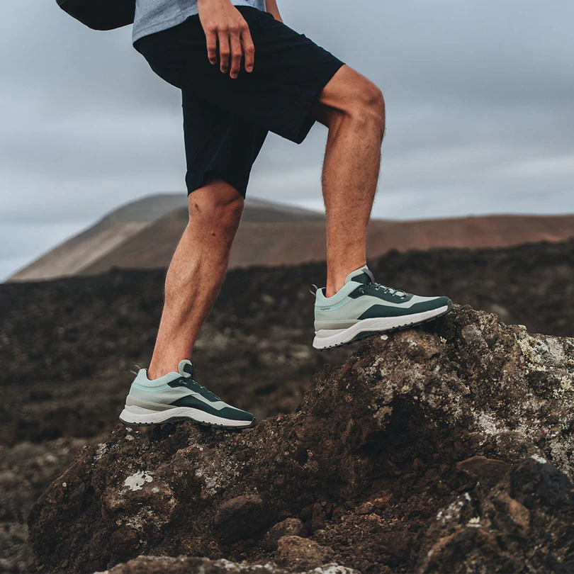 ethically made running shoes, person in grey and mint green shoes standing on a rock while hiking