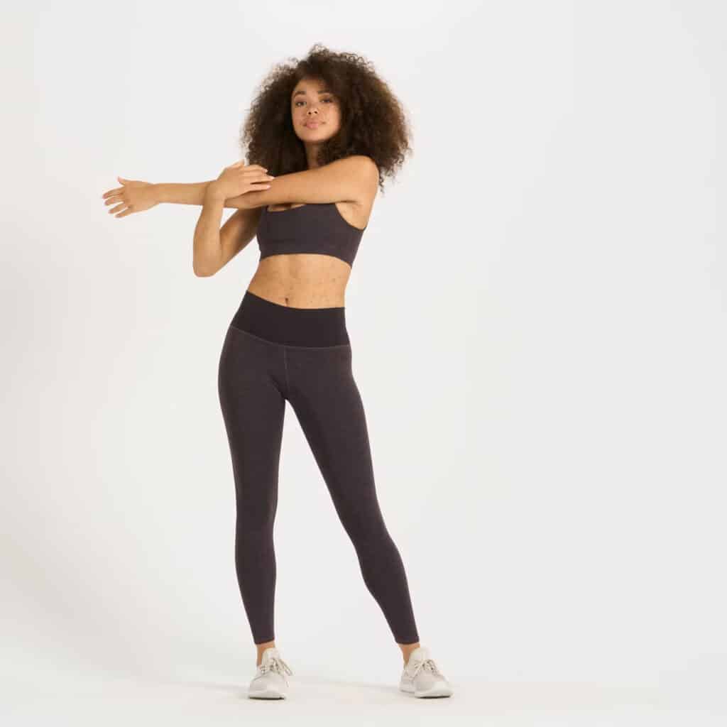 best sustainable leggings, woman in leggings and a bra stretching her arm