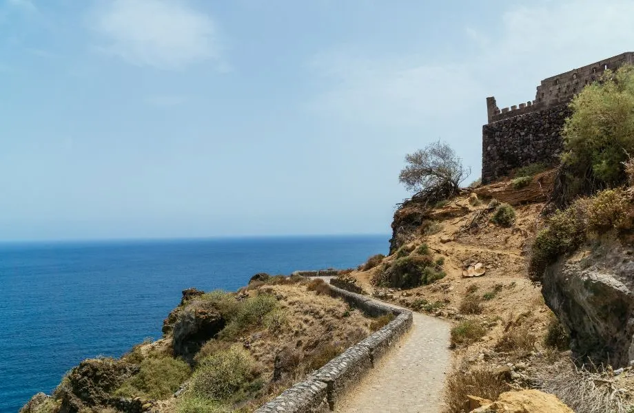 trekking in Tenerife, paved path winding along the coast with water on one side and stone building on the other