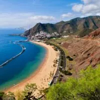 Amazing things to do in Tenerife, aerial view of beachy coast on a sunny day with mountains and a hillside village in the distance