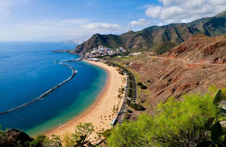 Amazing things to do in Tenerife, aerial view of beachy coast on a sunny day with mountains and a hillside village in the distance