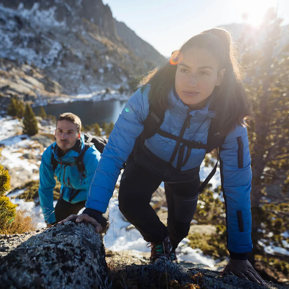 ethical winter coats, two people warm wearing coats hiking up mountain with lake and more mountains in background