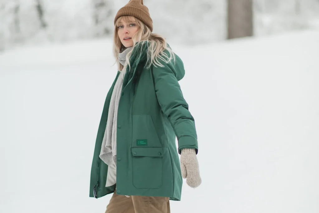 best sustainable parkas for winter, person wearing dark green jacket and long scarf and hat out on a snowy day