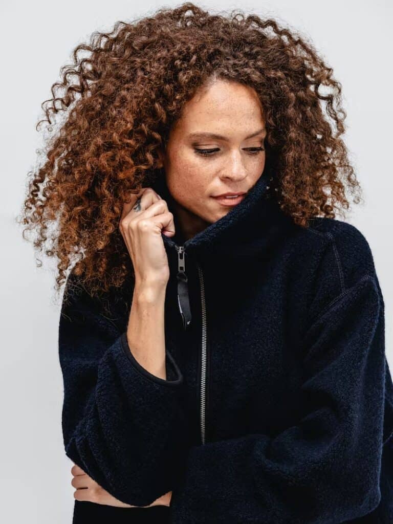 best eco-friendly winter coats, person with big hair cuddling up in warm winter coat