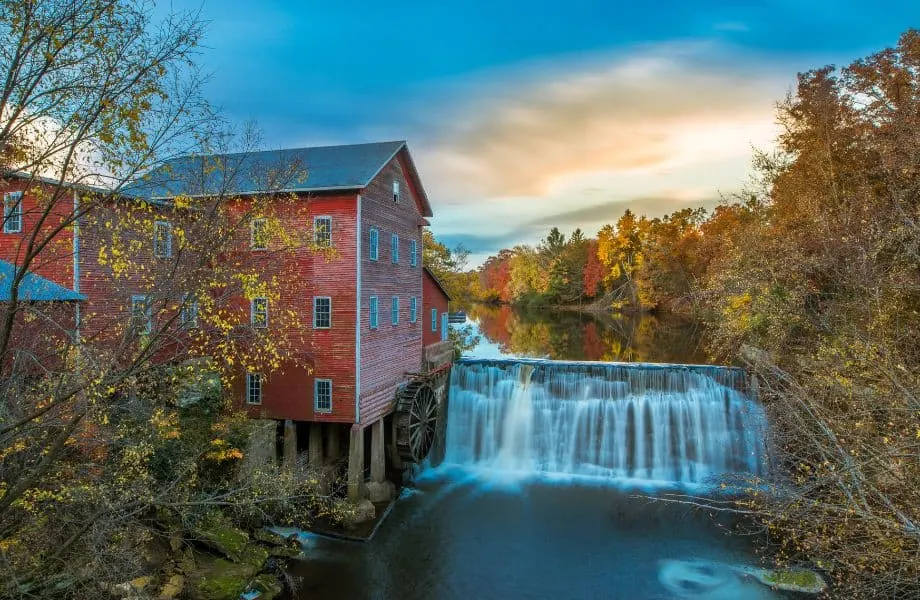 wooden mill next to waterfall and surrounded by fall colors at sunset