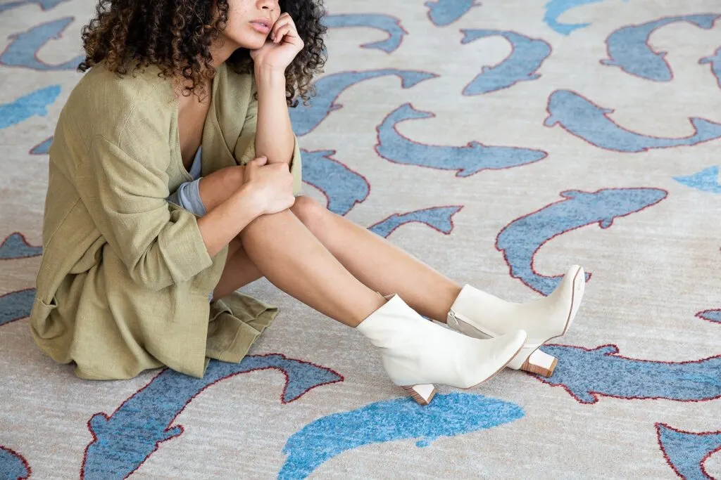 most sustainable boot brands, person sitting on rug with shark pattern wearing white boots with heel