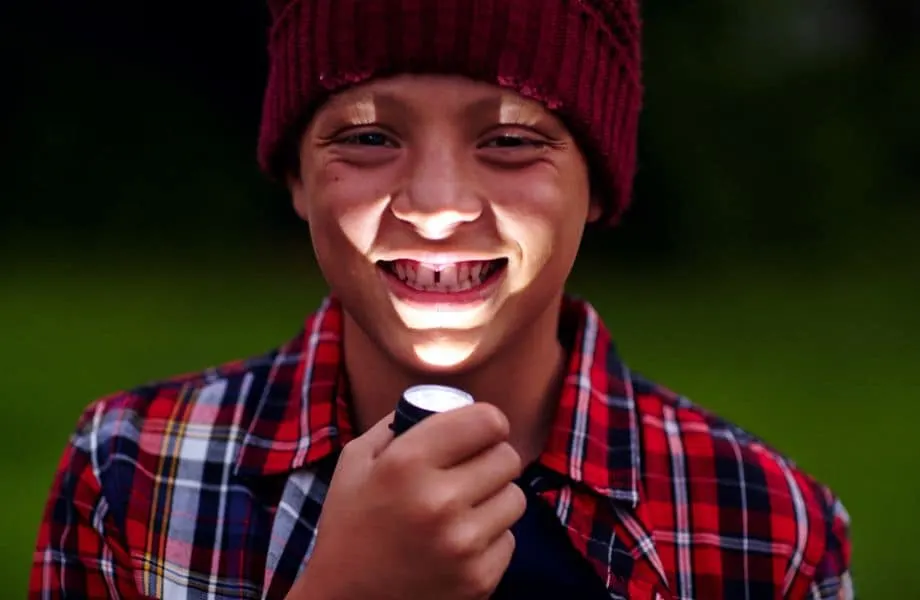 Take a haunted history tour in Appleton, smiling young boy in woolen hat and lumberjack checkered shirt holding flashlight under his chin