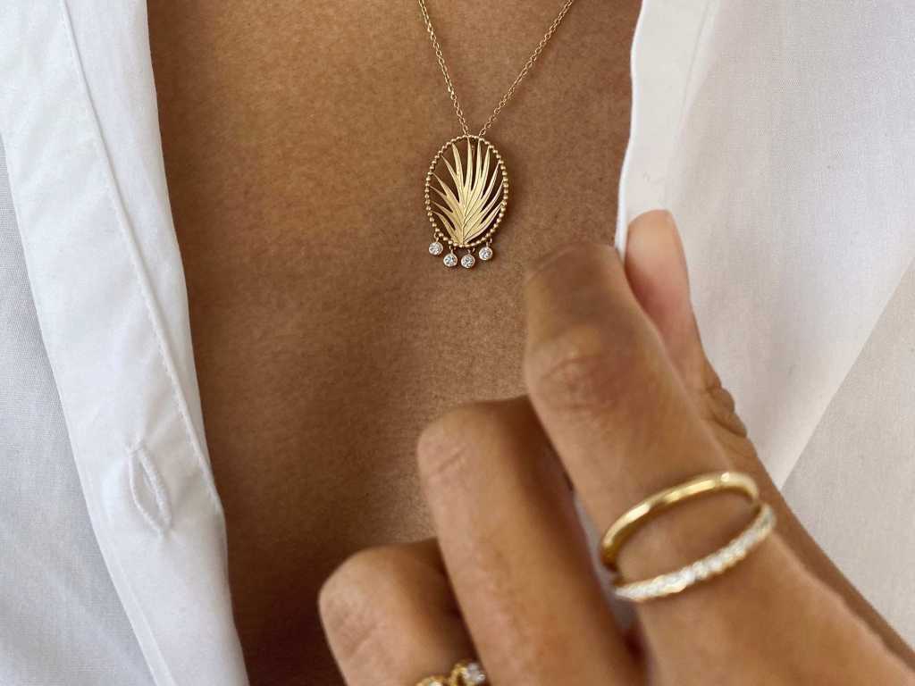 ethically sourced jewelry, person wearing necklace with leaf pendant and gold rings with fingers pulling back collar to showcase both items