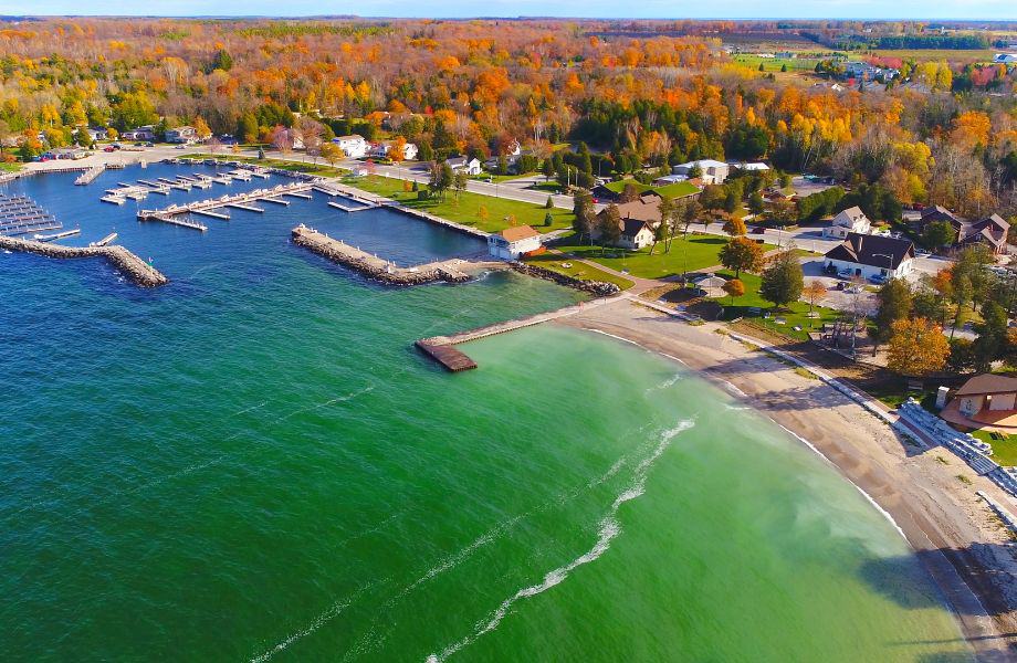 where to do in fall in Door County, aerial view of a coastal bay town surrounded on one side with bright green and blue waters and and on the other with miles of orange and yellow trees on a sunny day