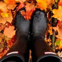 where to buy sustainable boots for every season, looking down at feet in Hunters rain boots in fallen autumn leaves
