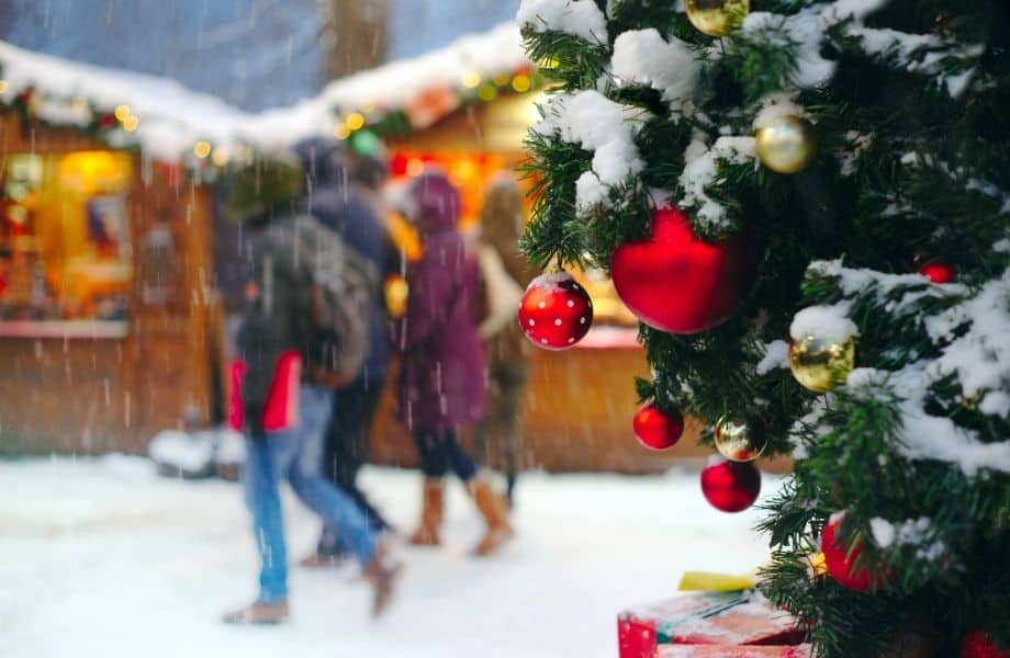 Top Christmas markets in Wisconsin, people walking in snow in front of market stalls in background with corner of Christmas tree in forefront